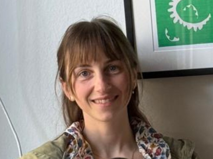 Hanna Malkwitz lächelt in die Kamera und sitzt in einem Büro vor einer hellen Wand.
